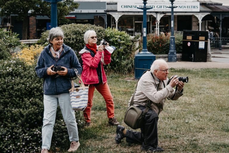 Group of senior tourists taking pictures in an urban park with cameras.